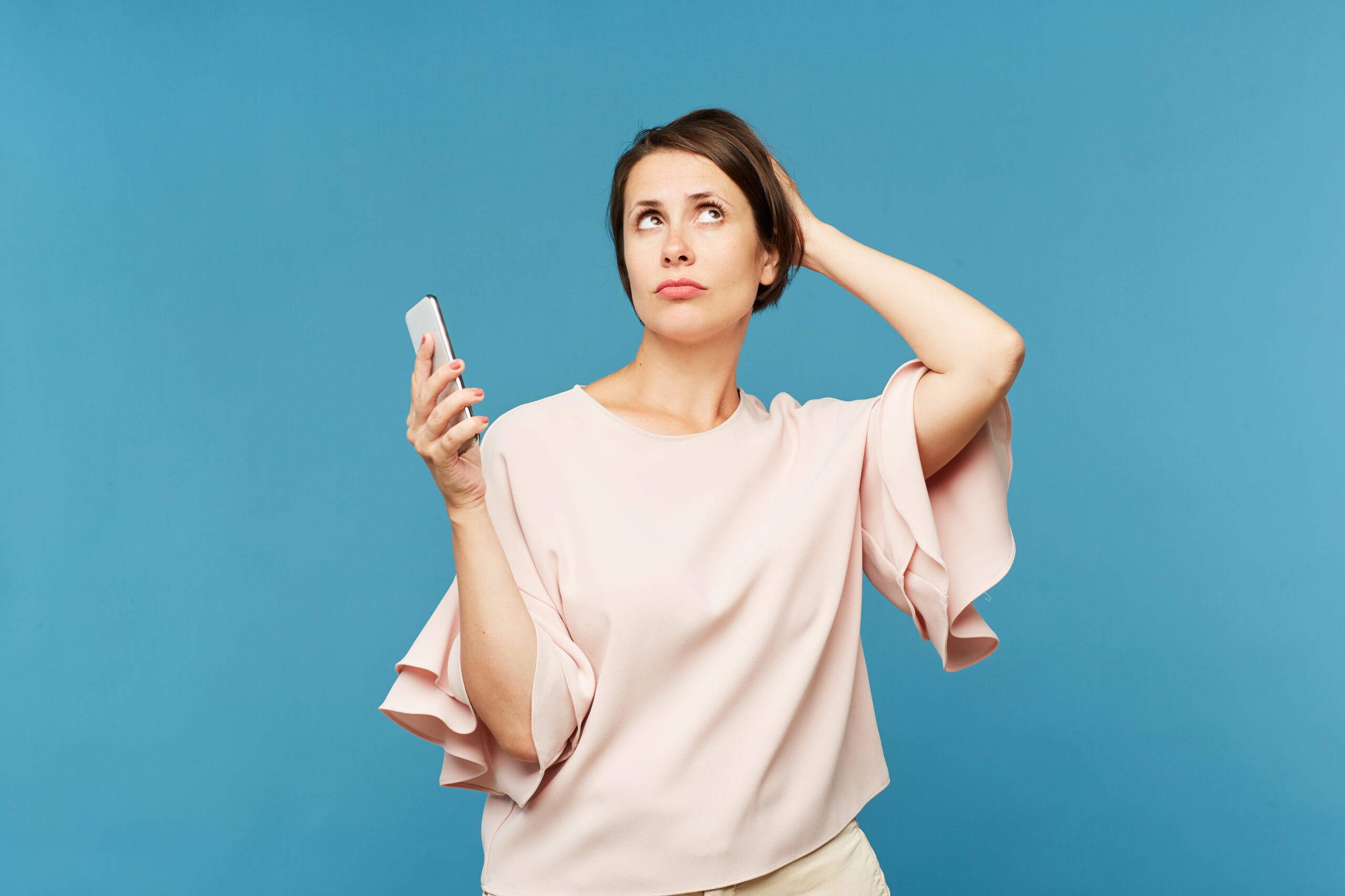 Young woman with smartphone speculating about promo or what to message while posing in isolation